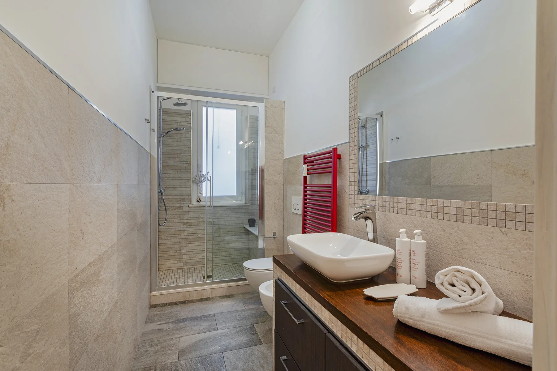 Un baño con una ducha de vidrio, un lavabo y un espejo grande.