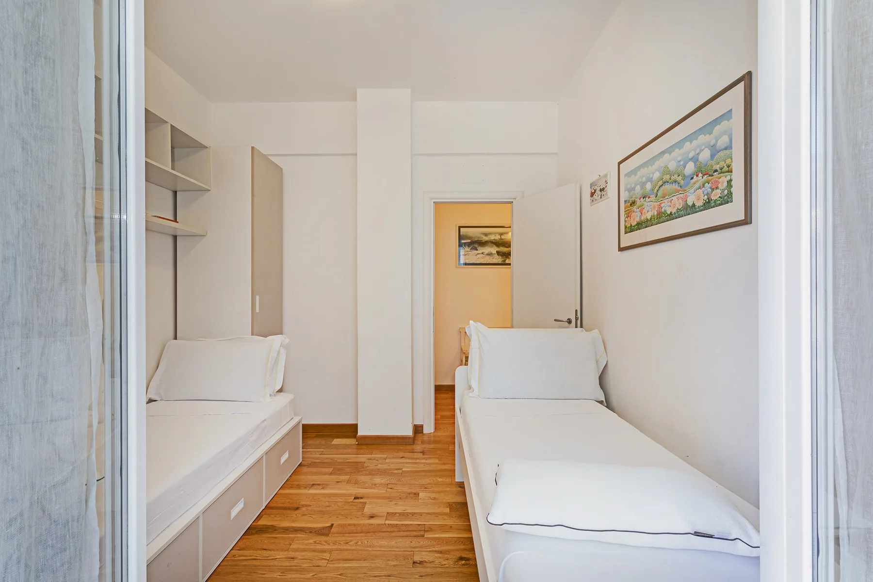 Un dormitorio luminoso con dos camas individuales y suelo de madera.