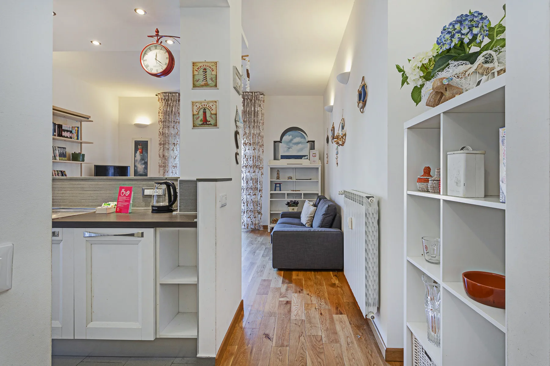 Una pequeña zona de estar con cocina, asientos y estanterías blancas.