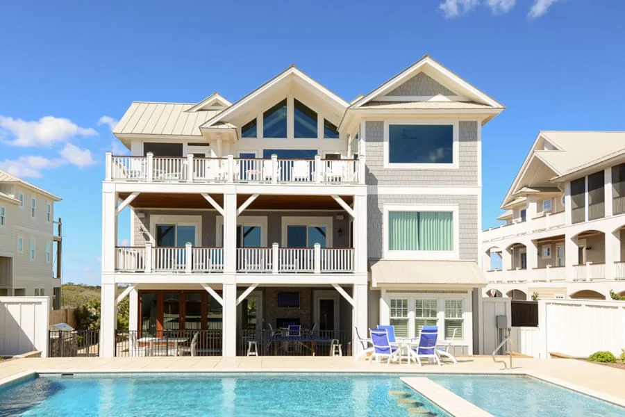 Una casa grande de estilo costero con balcones está junto a una piscina.