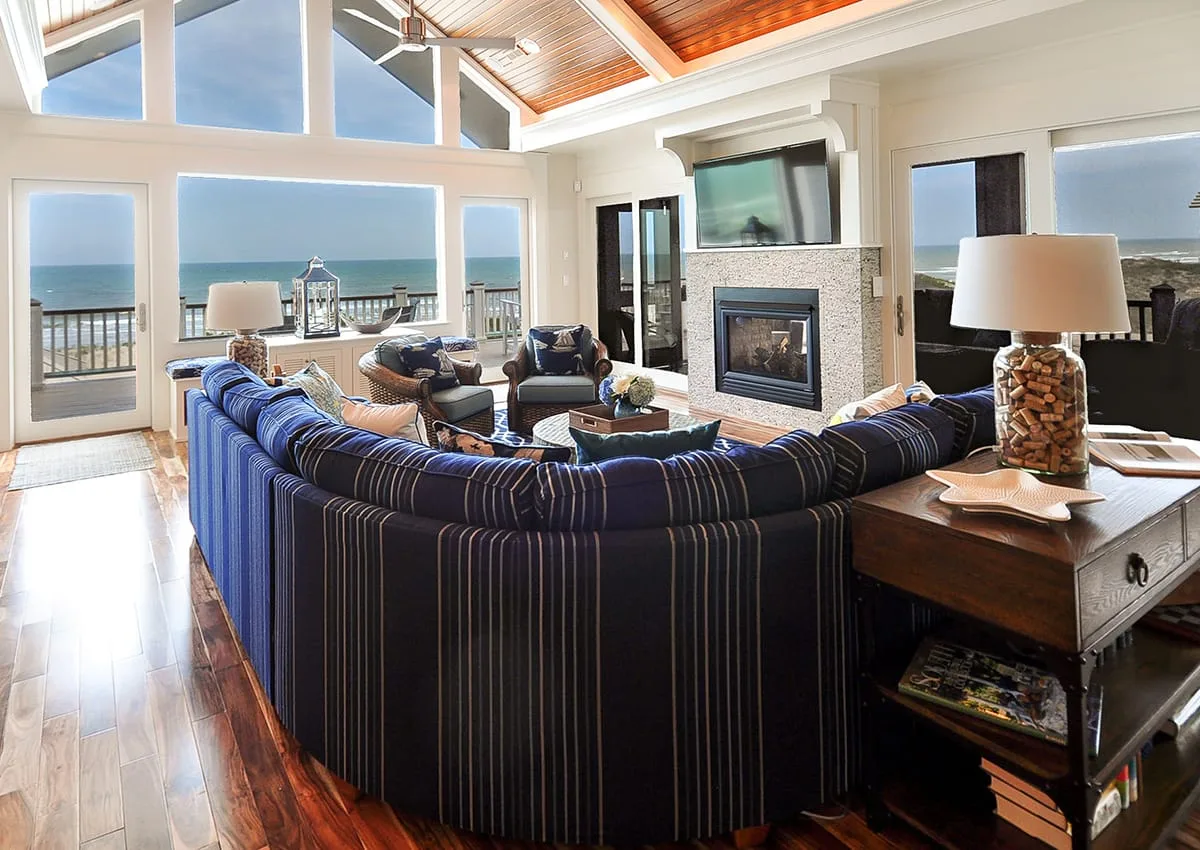 Una sala luminosa con asientos a rayas, una chimenea y vistas al mar por grandes ventanales.