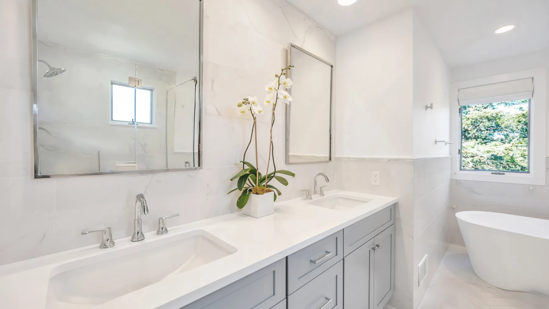 Un baño luminoso tiene un largo tocador blanco con dos lavabos y una bañera exenta.