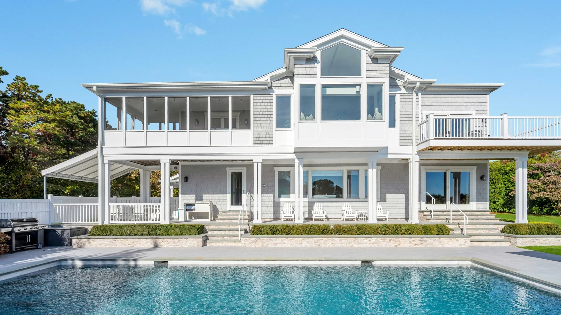 Una casa blanca grande con amplias ventanas se alza detrás de una piscina.