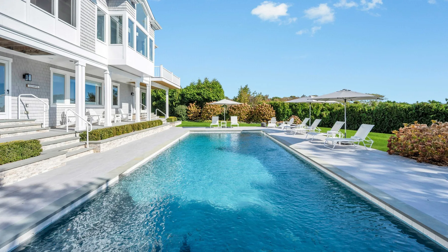 Piscina al aire libre junto a un edificio blanco, con tumbonas alrededor.