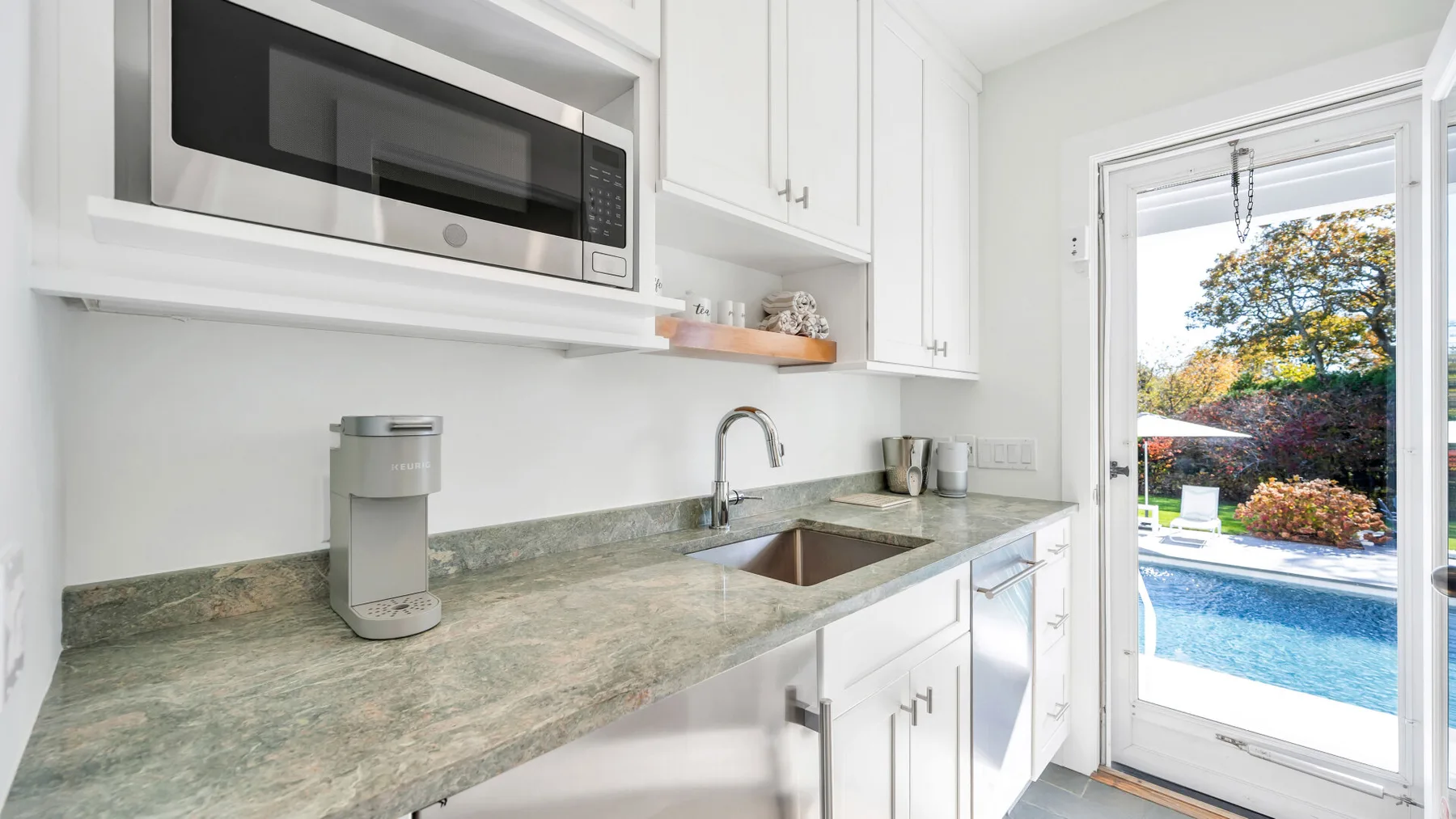 Una cocina luminosa con encimera, fregadero y puerta de vidrio con vista a una piscina.