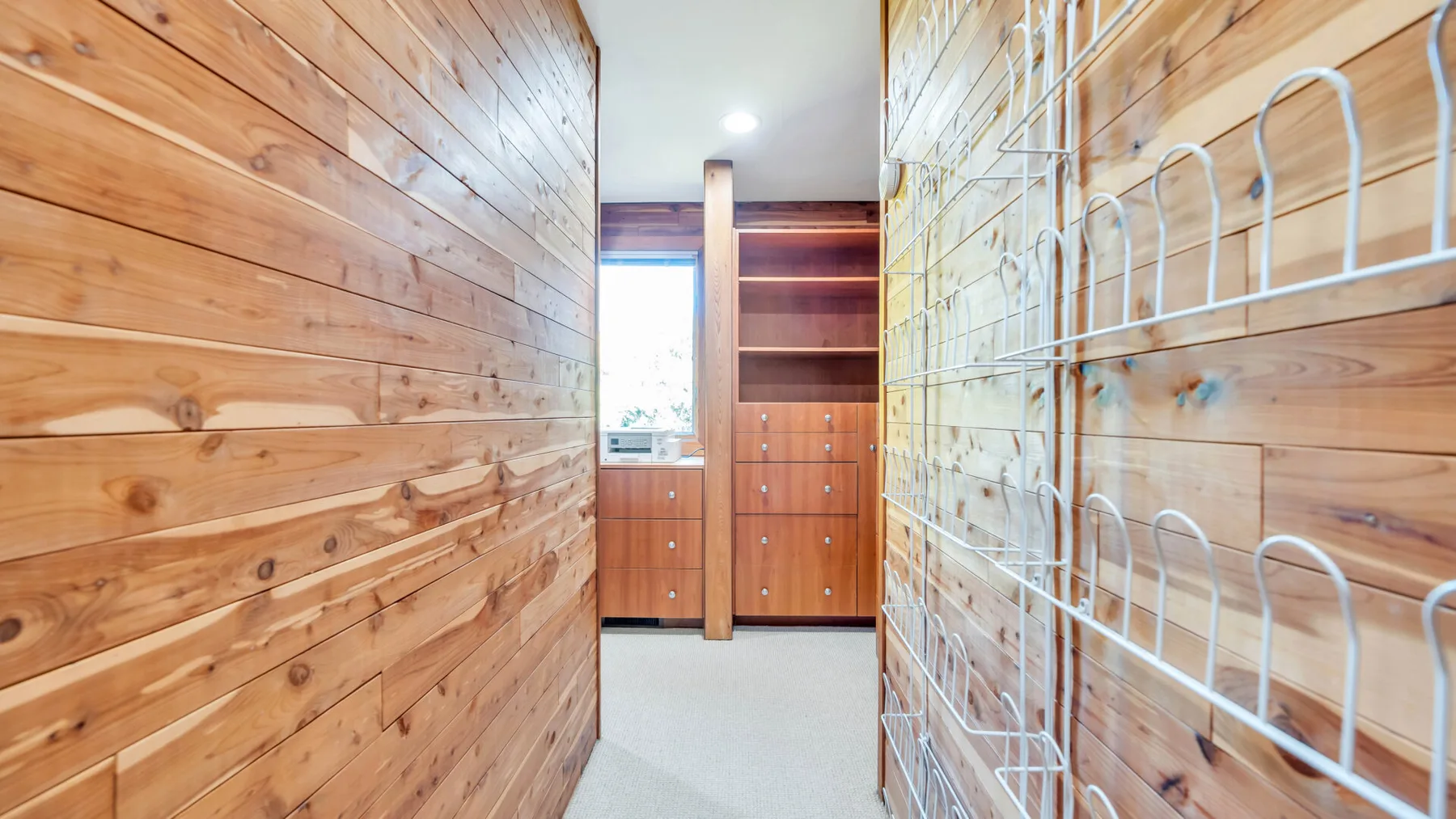 Una habitación estrecha revestida de madera, con literas metálicas y armarios empotrados.