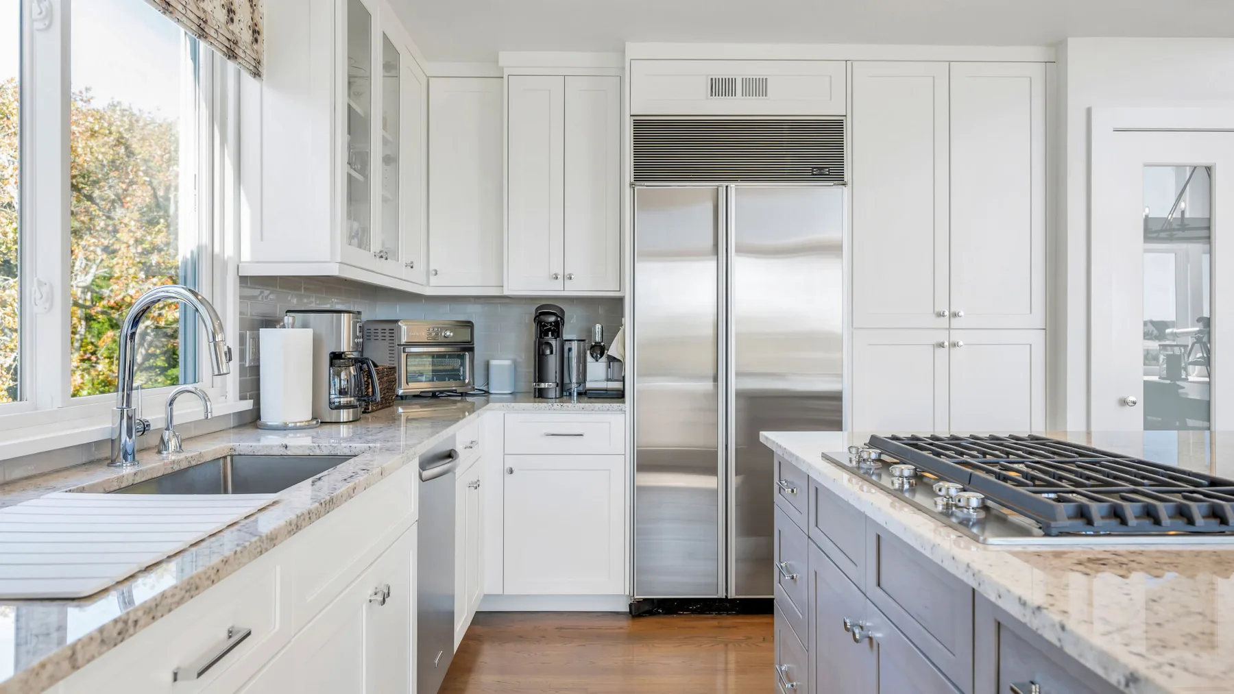 Una cocina luminosa con gabinetes blancos, un refrigerador de acero inoxidable y una isla grande.