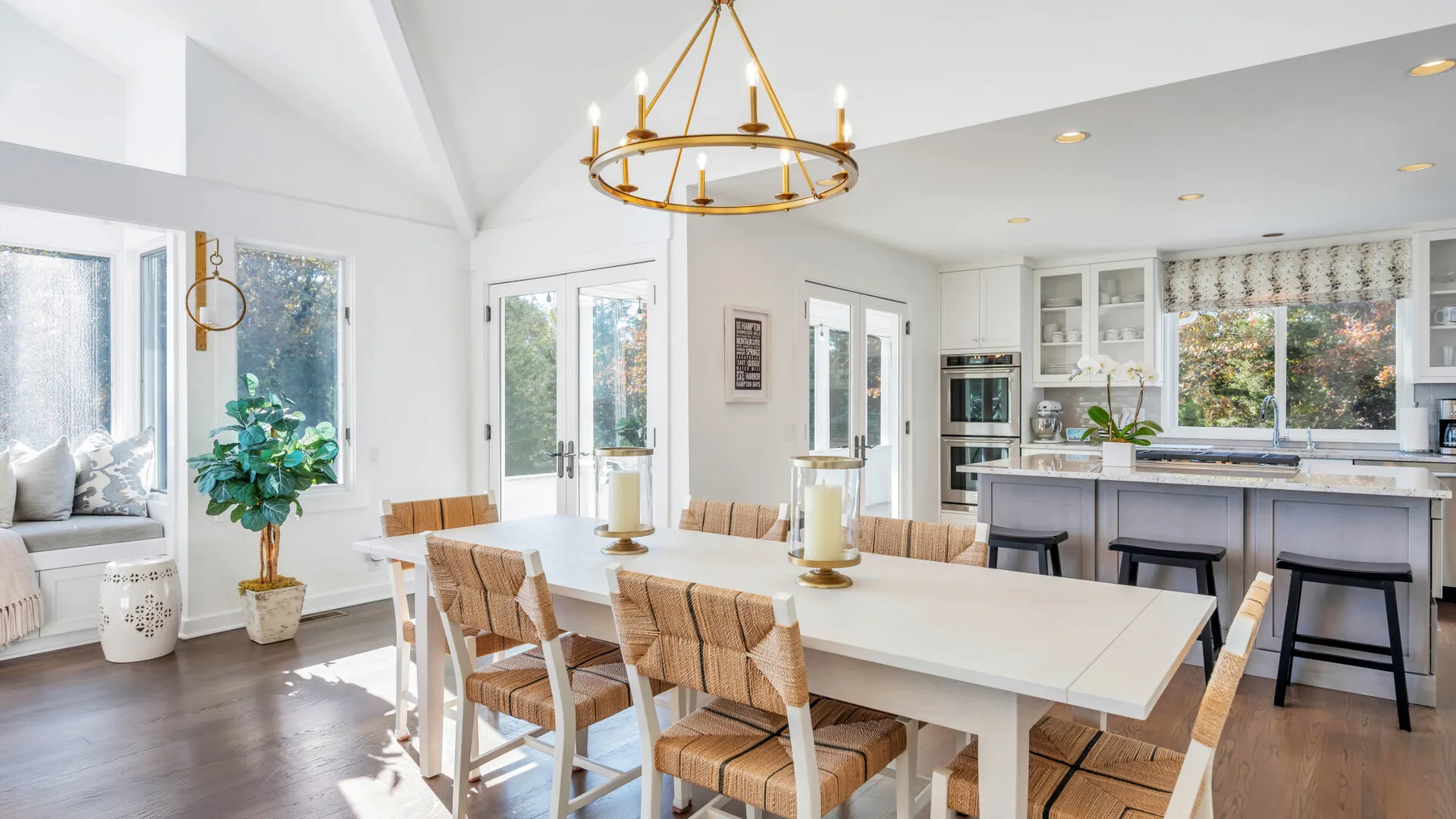 Un comedor luminoso con una mesa larga, asientos tejidos y grandes ventanas.