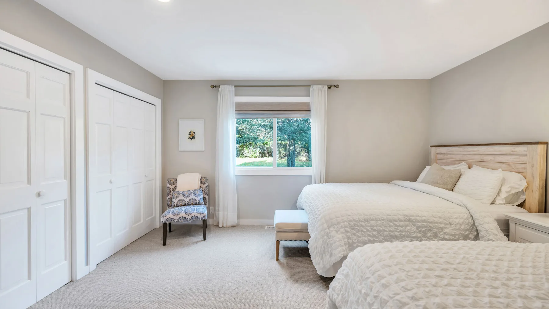 Un dormitorio luminoso con camas, una ventana y un pequeño asiento tapizado.