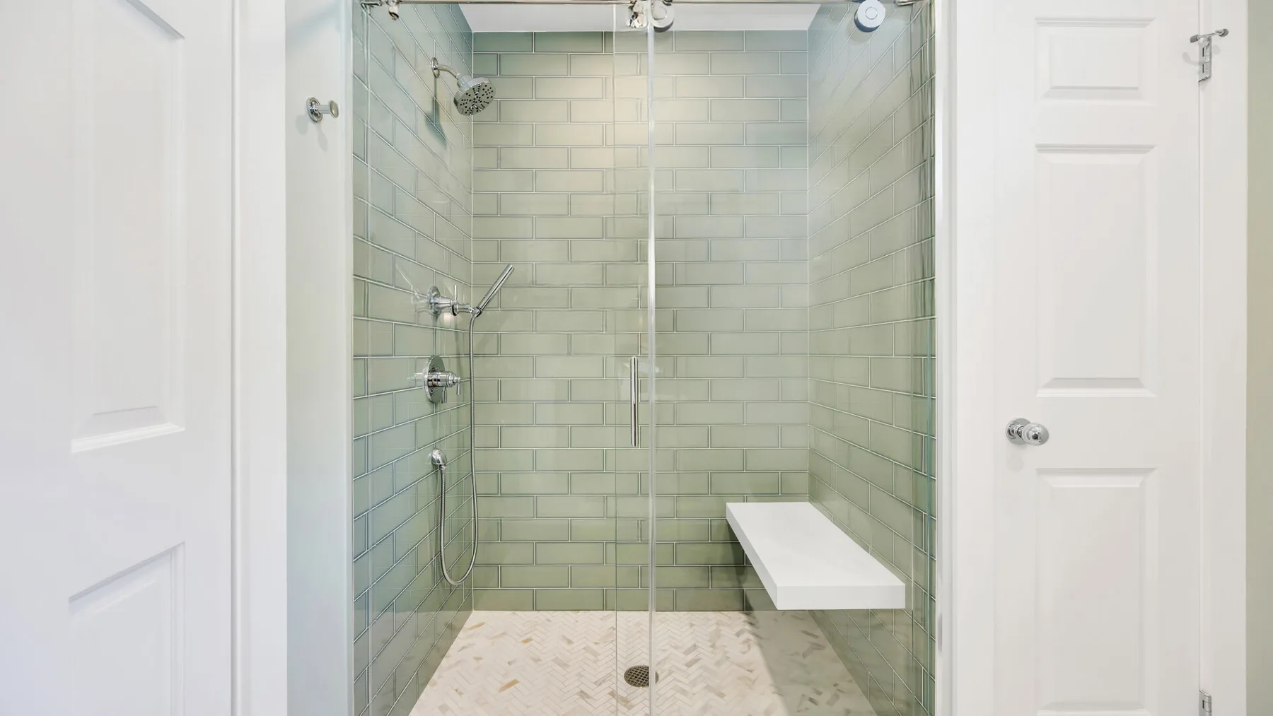Una ducha con azulejos, mampara de vidrio y un banco incorporado.
