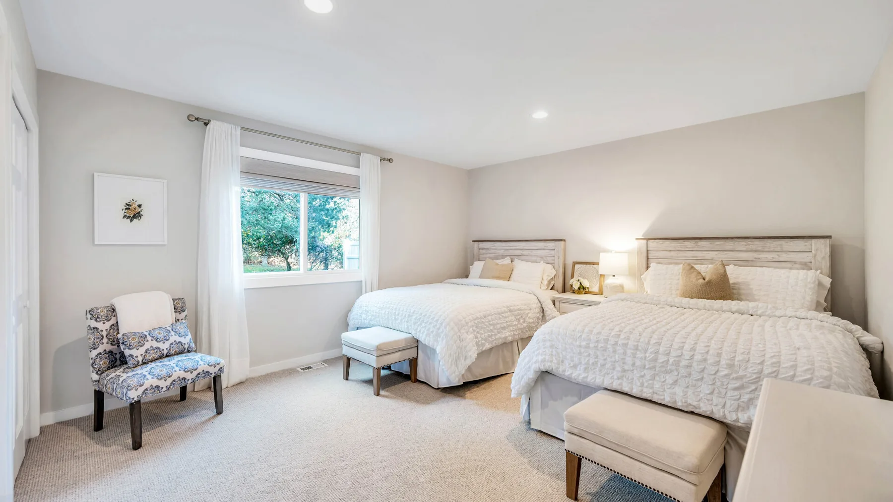 Un dormitorio luminoso con dos camas y una ventana con cortinas blancas.