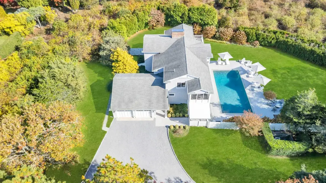 Vista aérea de una casa junto a una piscina, rodeada de césped y árboles.