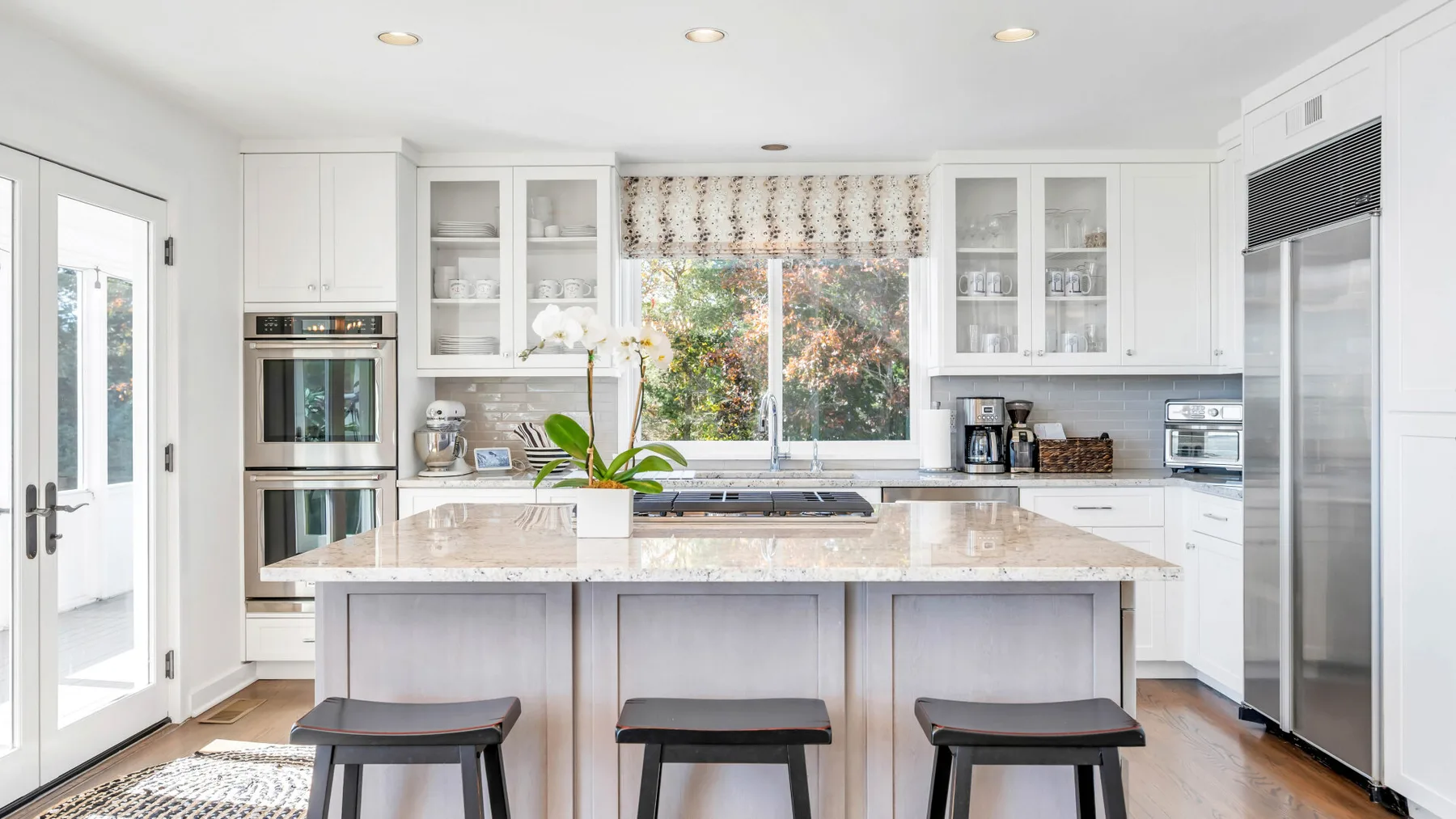 Una cocina blanca y luminosa con una isla central y grandes ventanas.