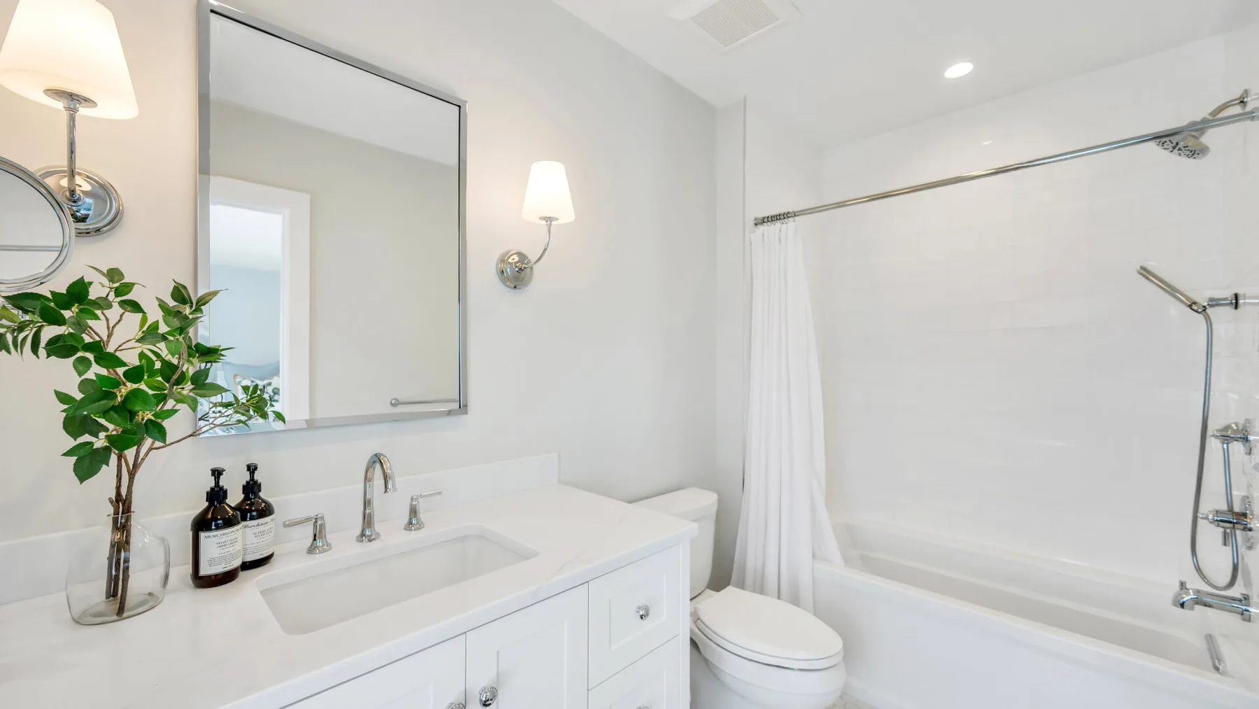 Un baño luminoso con lavabo, espejo, inodoro y bañera con ducha.