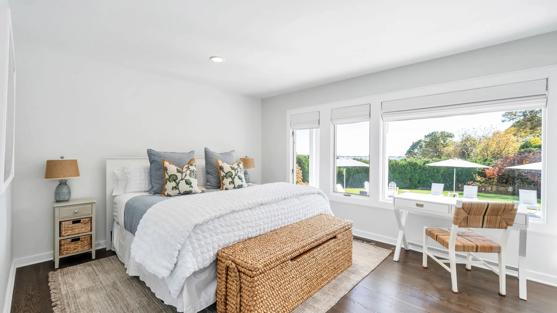 Un dormitorio luminoso con una cama bien arreglada y una pequeña zona de estar junto a las ventanas.