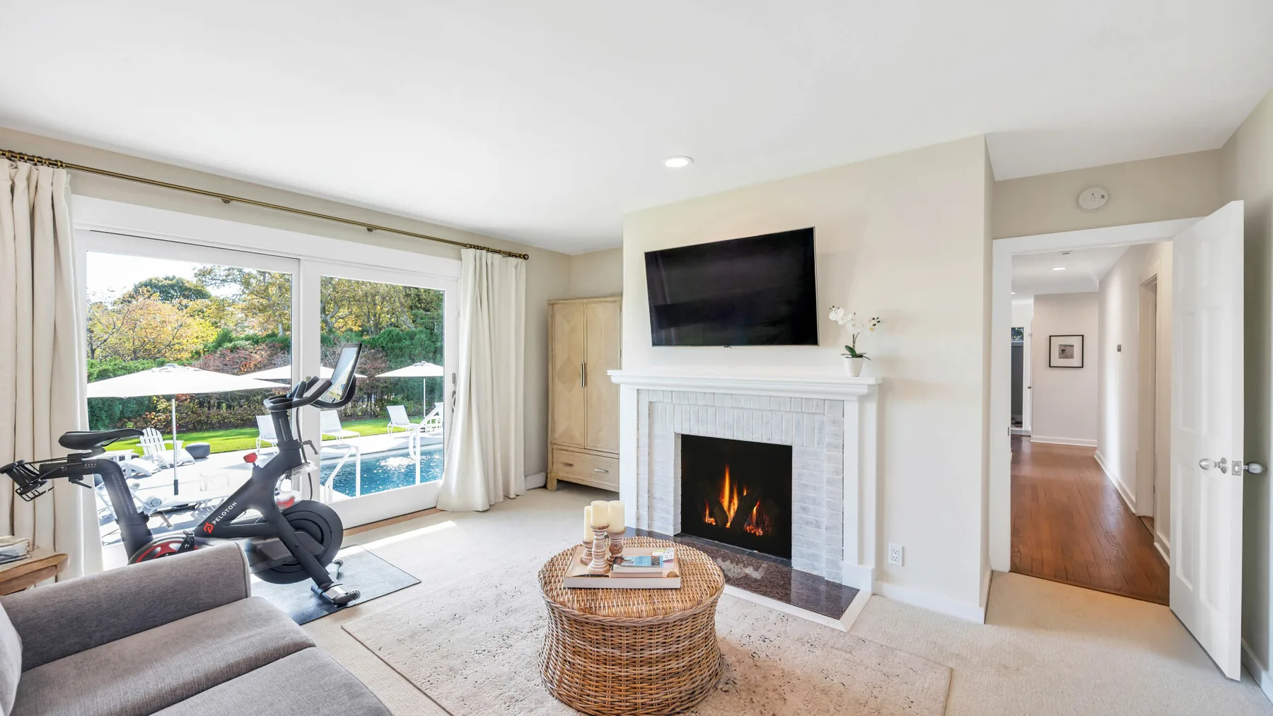 Una sala luminosa con chimenea, televisor y equipo de ejercicio junto a la ventana.