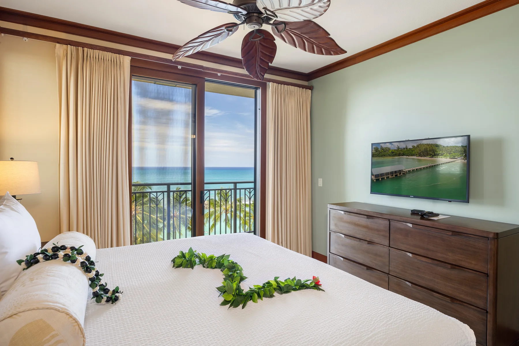 Un dormitorio con una cama, una cómoda y un televisor junto a una ventana con balcón.