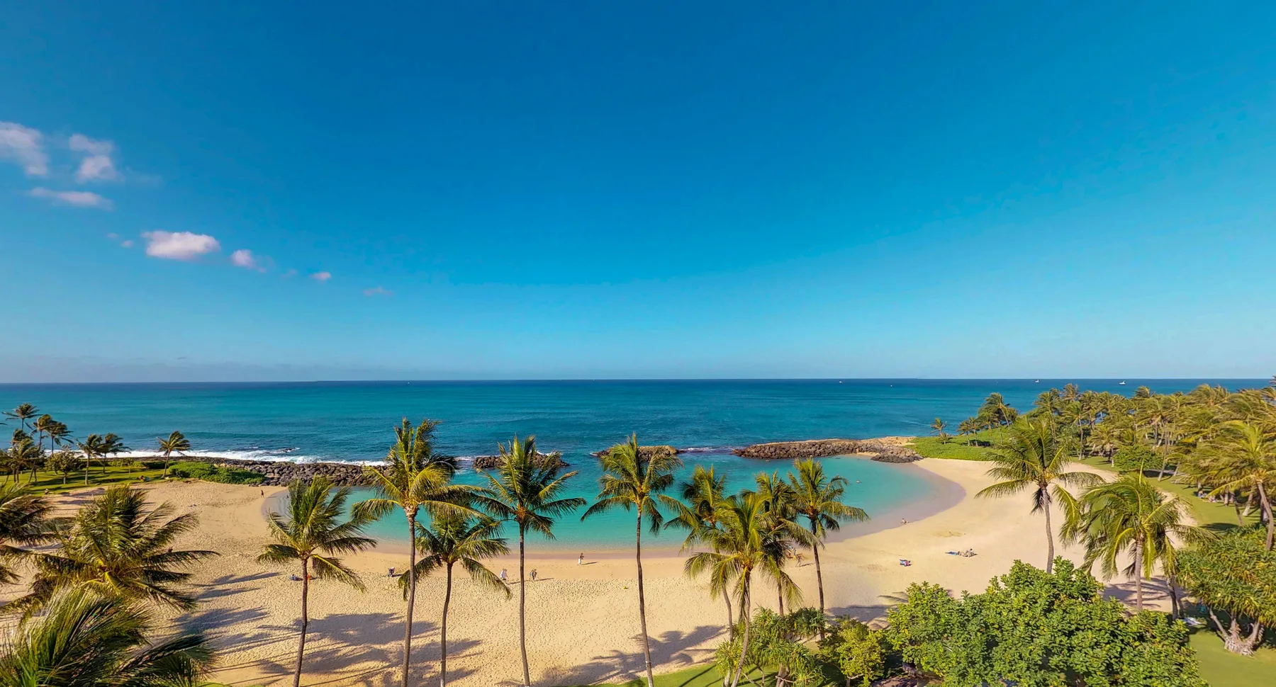 Una playa de arena con palmeras bordea una bahía turquesa tranquila.