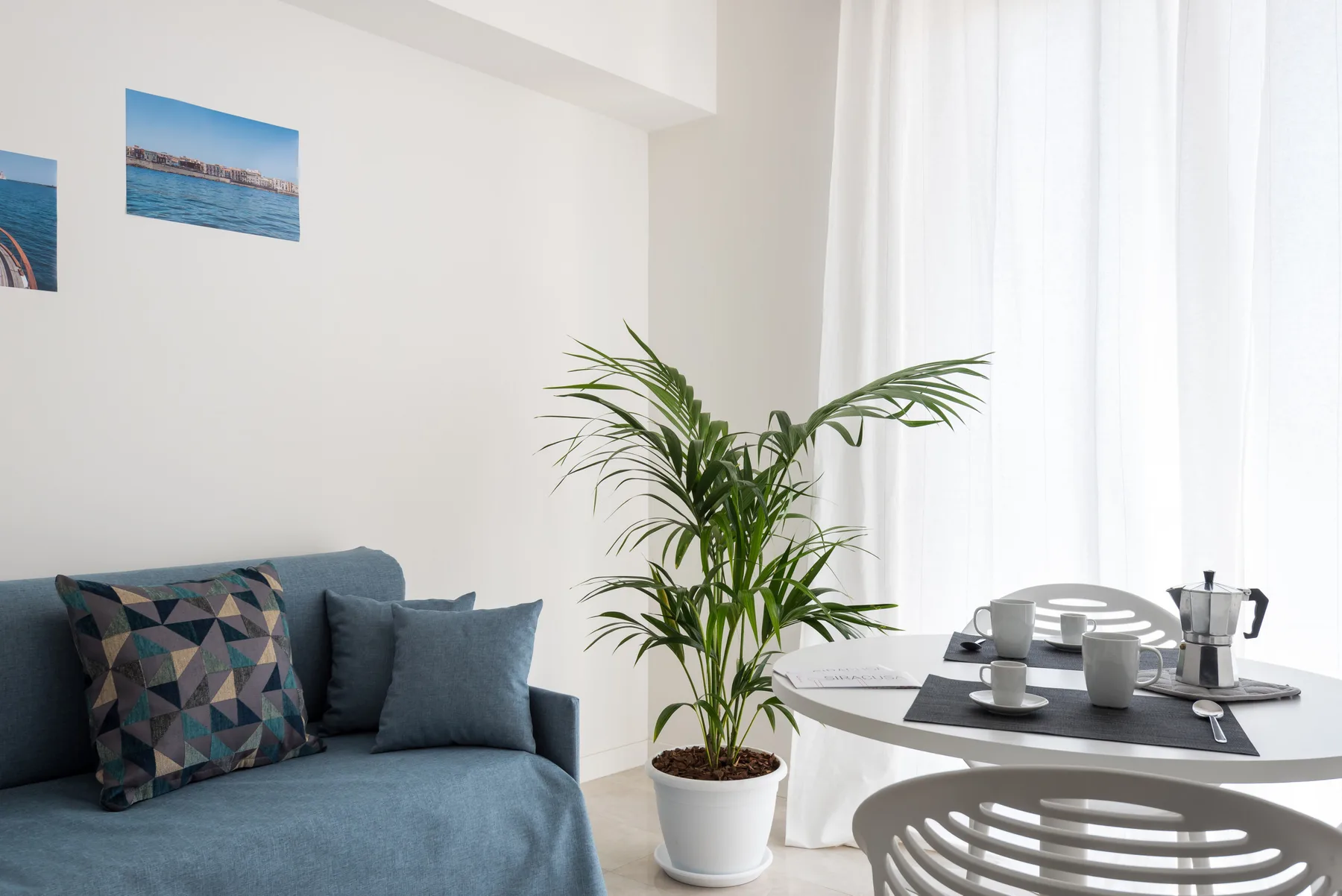 A bright living and dining area with blue seating, a dining table, and a potted plant.