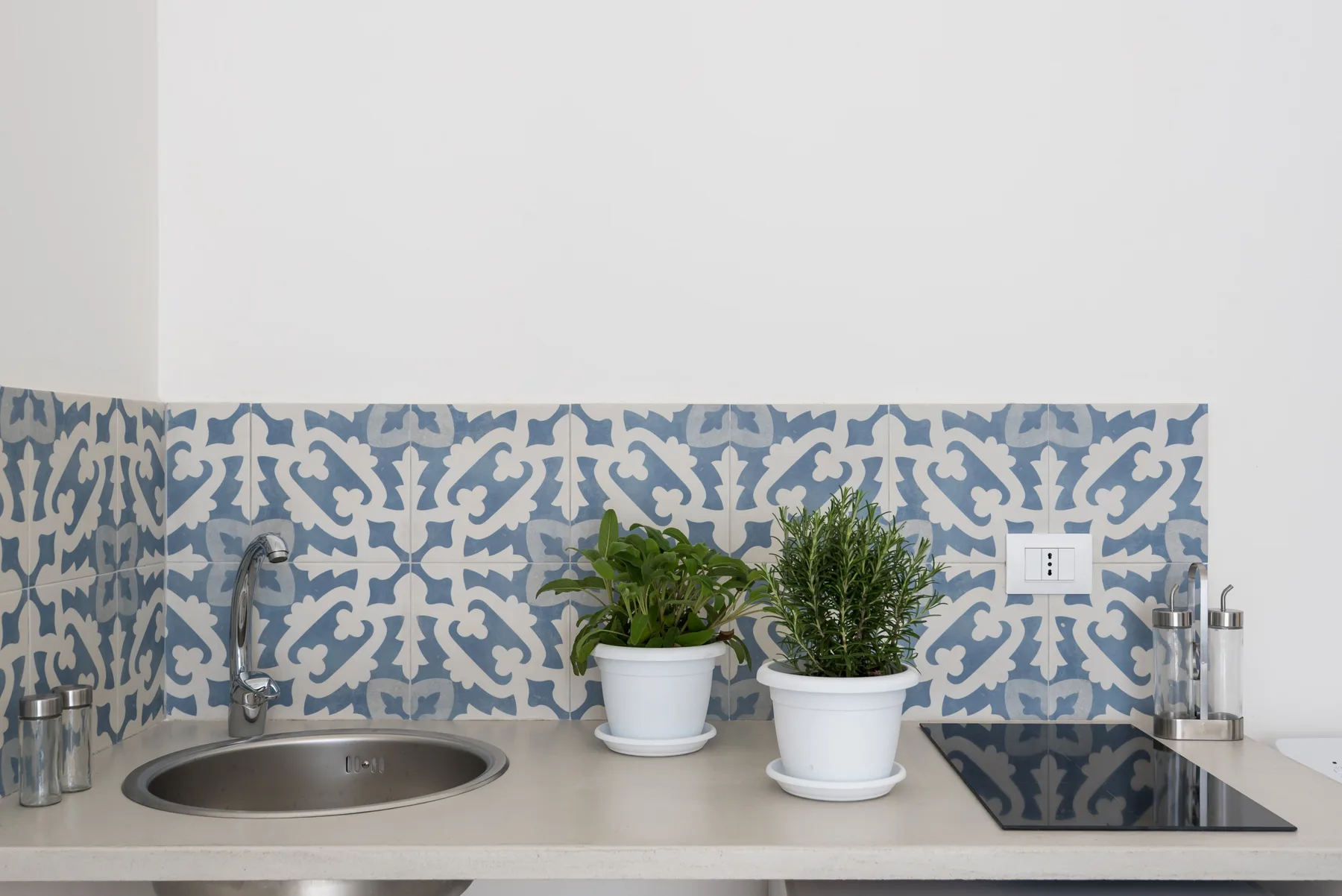 A tiled kitchen counter with a sink, cooktop, and potted plants.