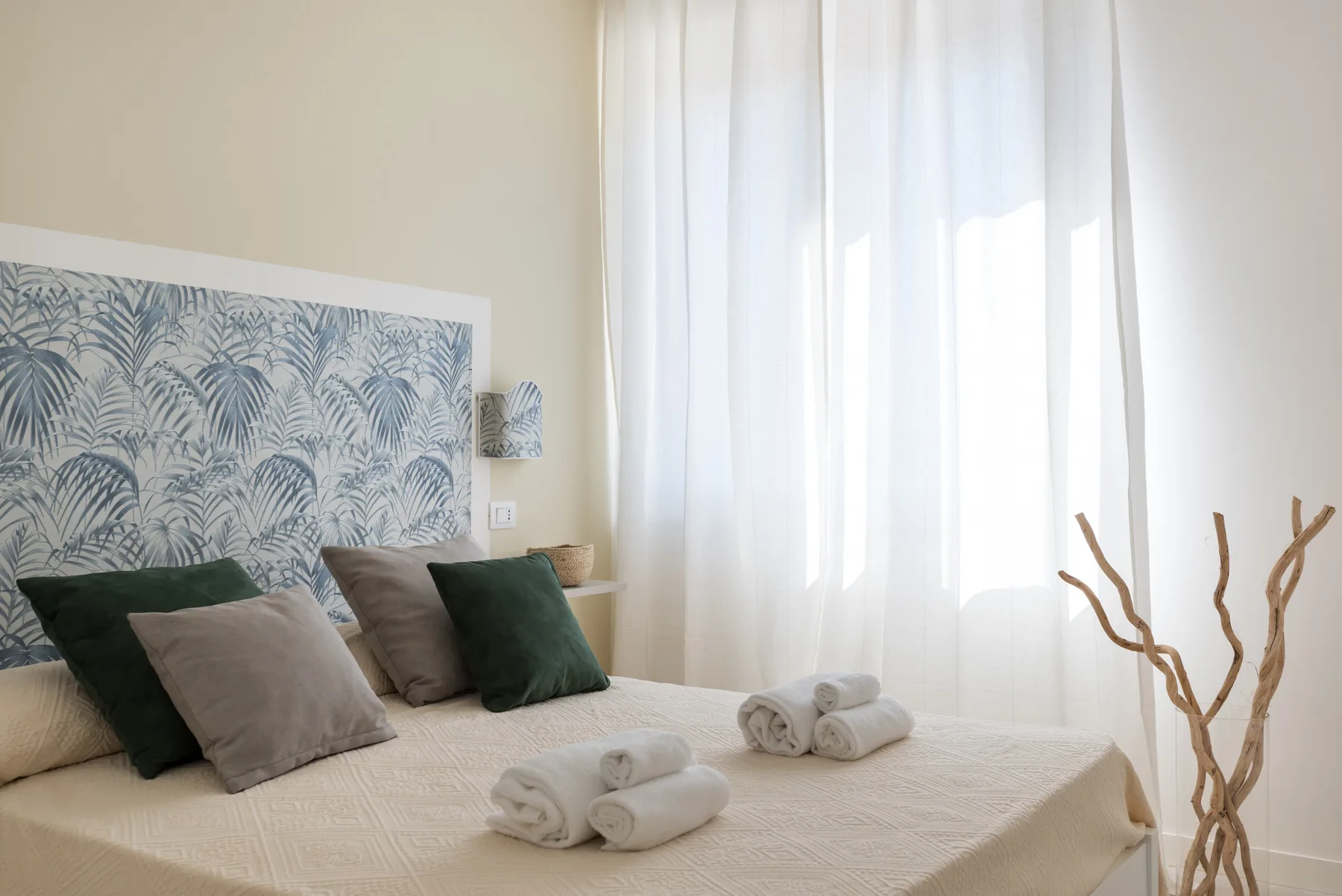 A bedroom with a neatly made bed, decorative pillows, and sheer curtains.