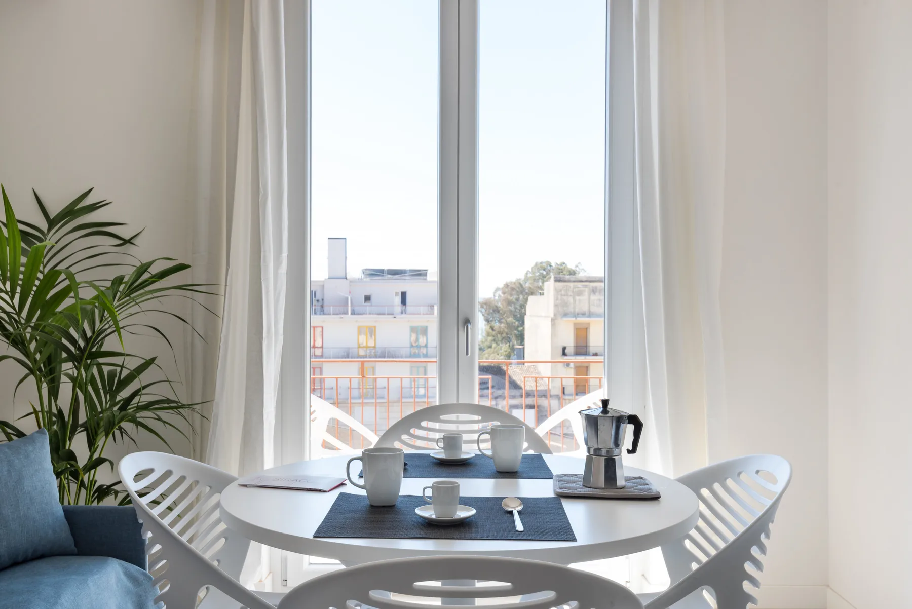 A bright dining area with a round table and large window overlooking nearby buildings.