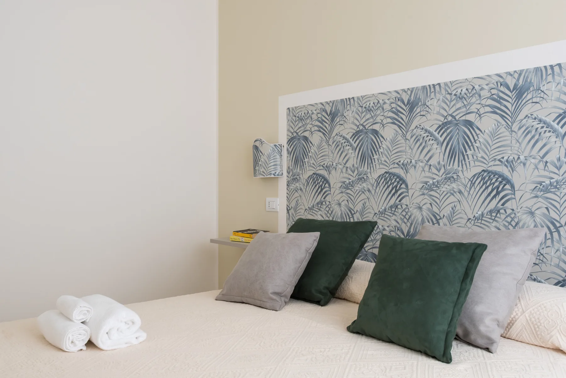A bedroom with a neatly made bed and patterned wallpaper behind the pillows.