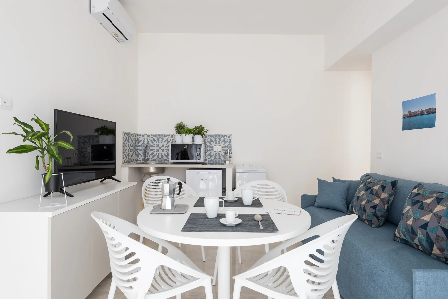 Dining area with white table and chairs beside a blue sofa and television.
