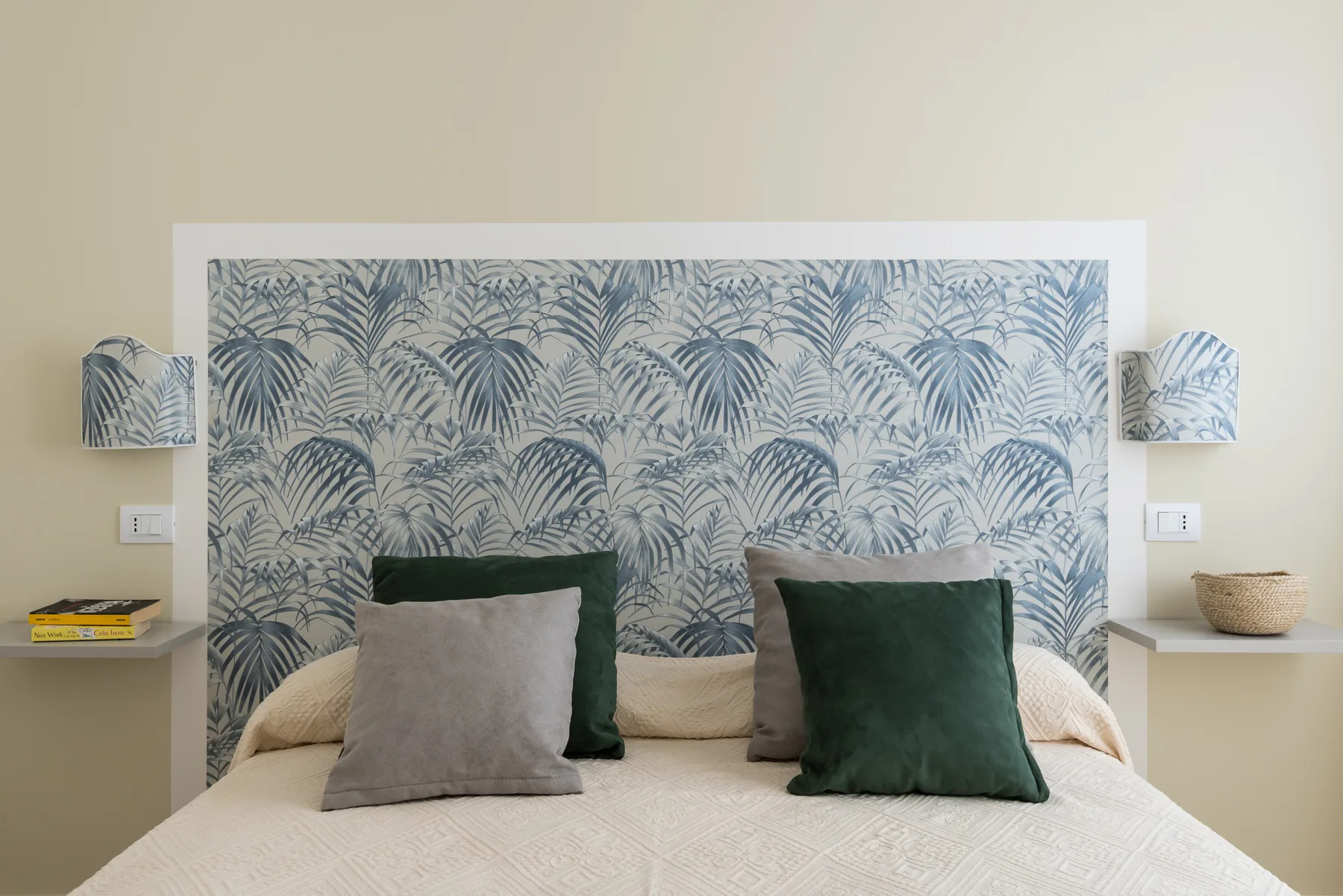 A bedroom with a bed against a patterned botanical wall.