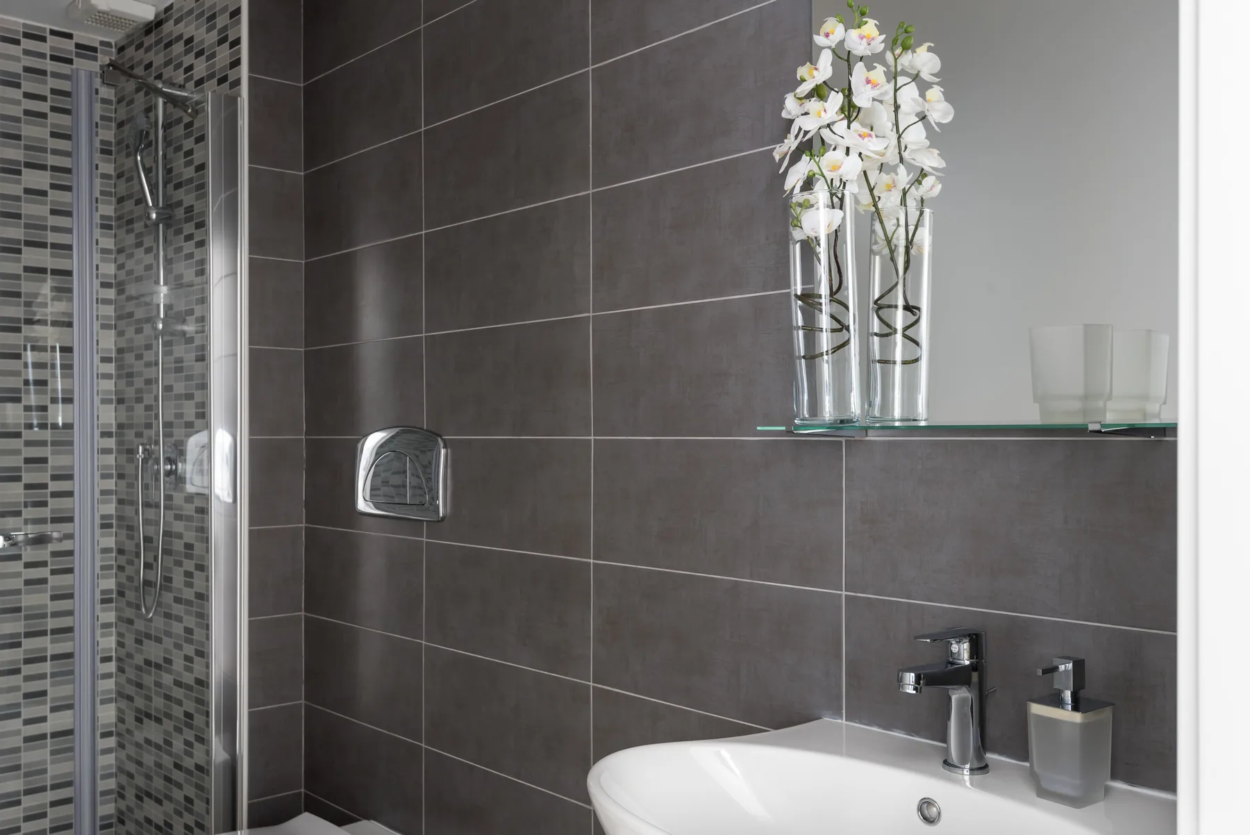 A modern bathroom with a tiled shower and a white sink.