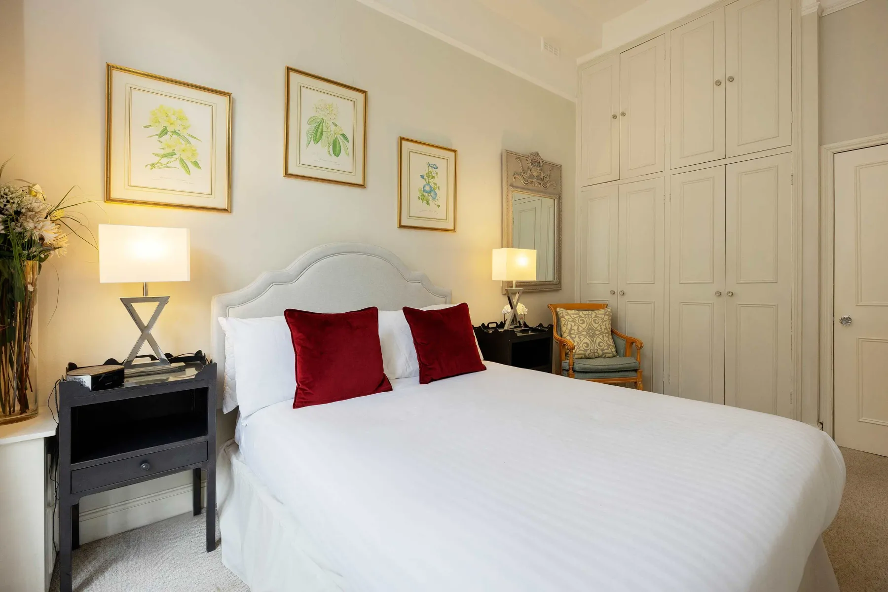 Un dormitorio luminoso con una cama bien hecha, cojines rojos y armarios empotrados.