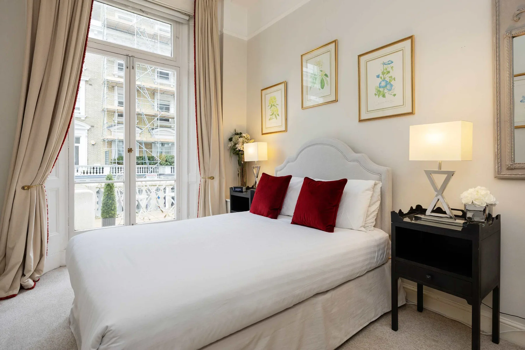 Un dormitorio luminoso con una cama grande, cojines rojos y ventanas altas.
