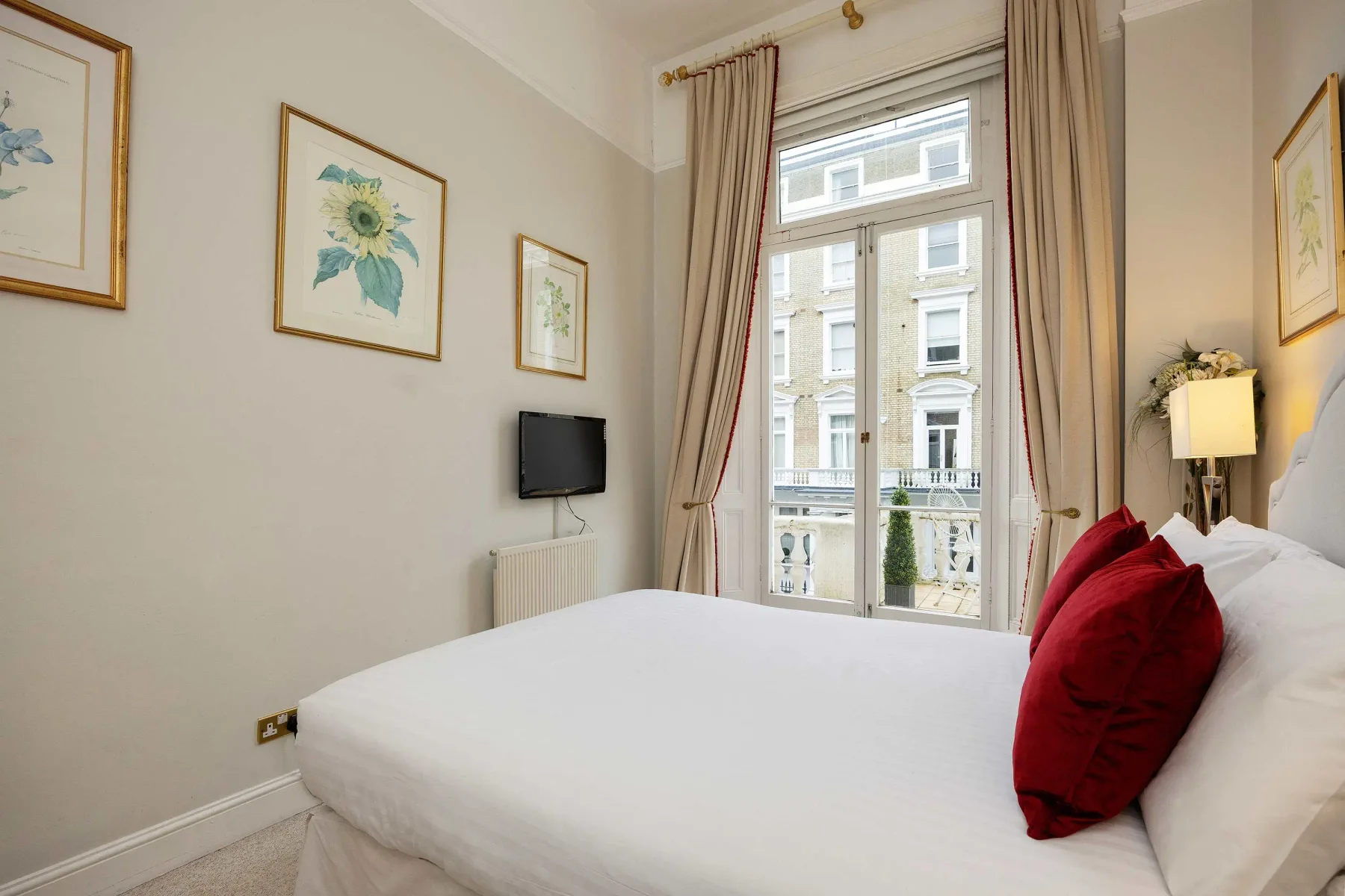 Dormitorio con una cama grande, cojines rojos y una ventana alta.