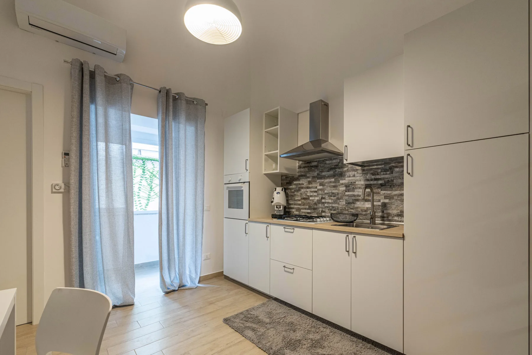 A compact kitchen with white cabinets, a cooktop, and a dining chair.
