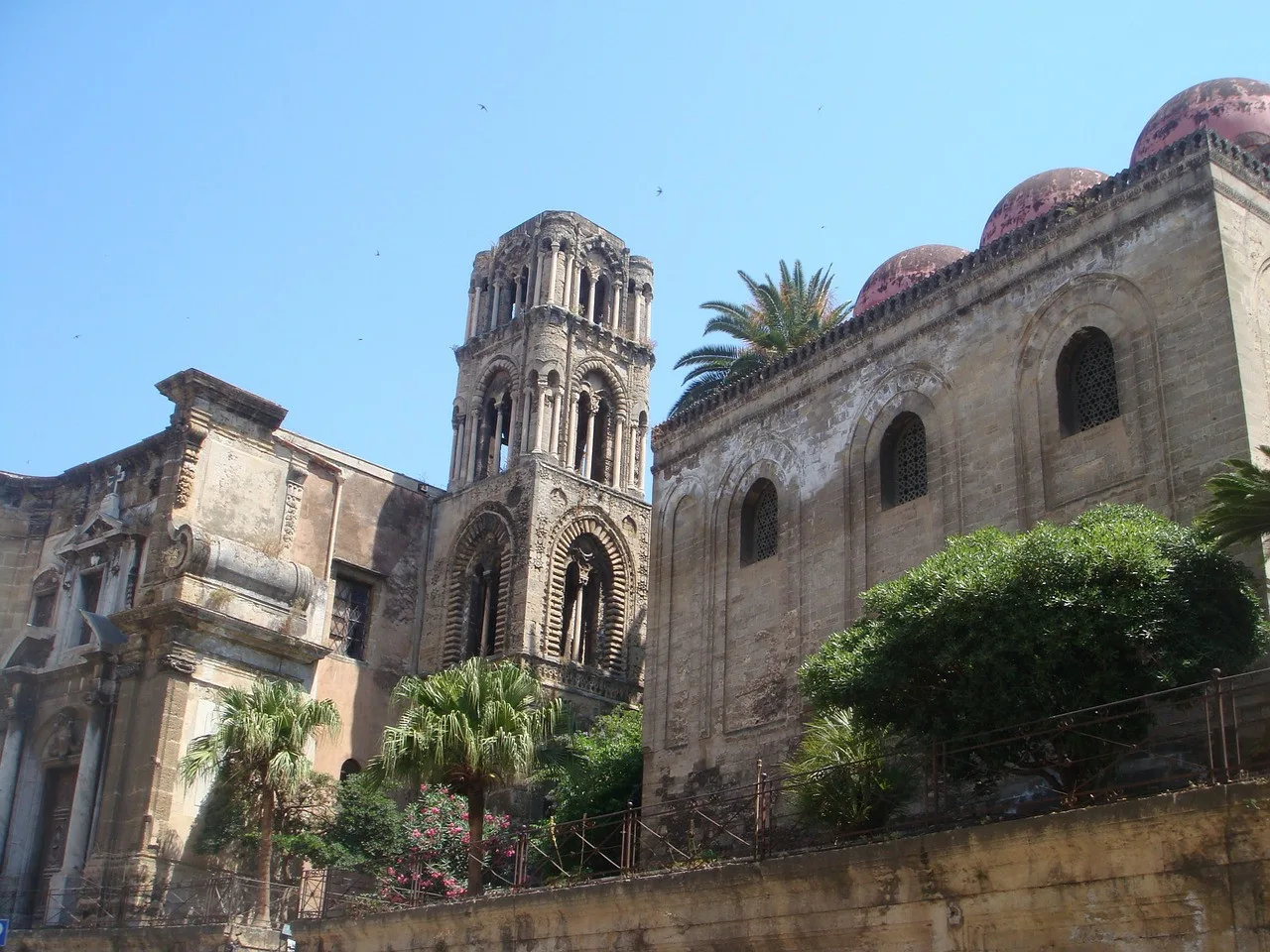 A historic stone church complex with an ornate bell tower and greenery in front.