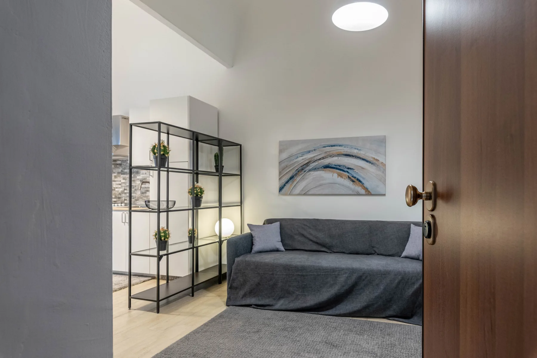 A bedroom with a gray bed, an open shelving unit, and abstract wall art.