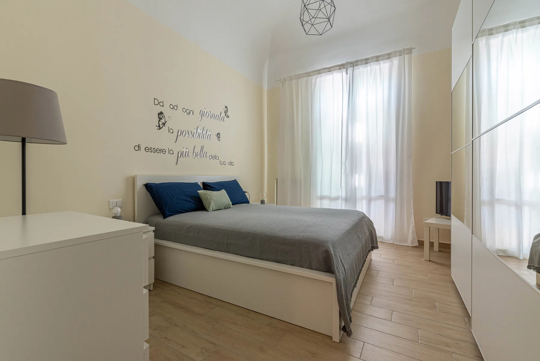 A bedroom with a bed, a dresser, and a large curtained window.