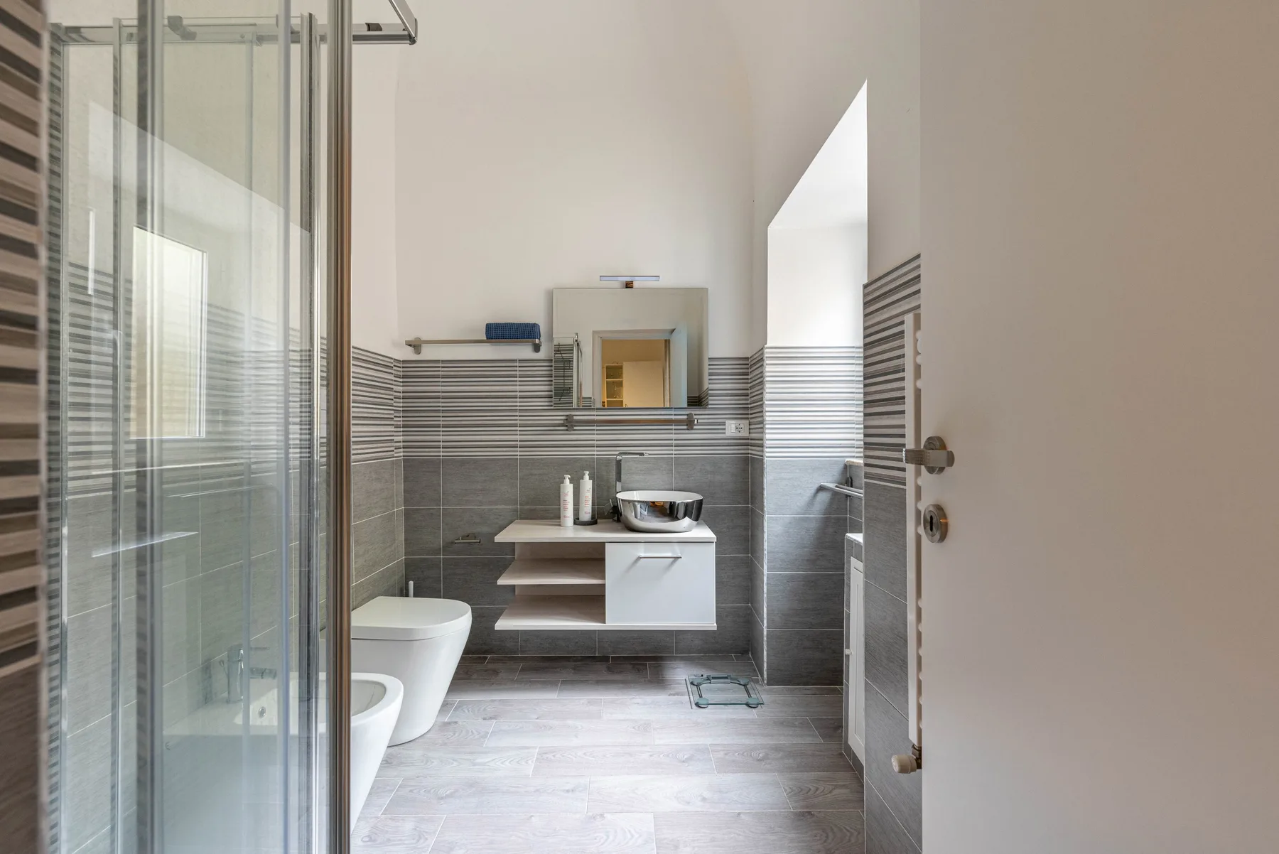 A modern bathroom with a glass shower, wall-mounted sink, and toilet.