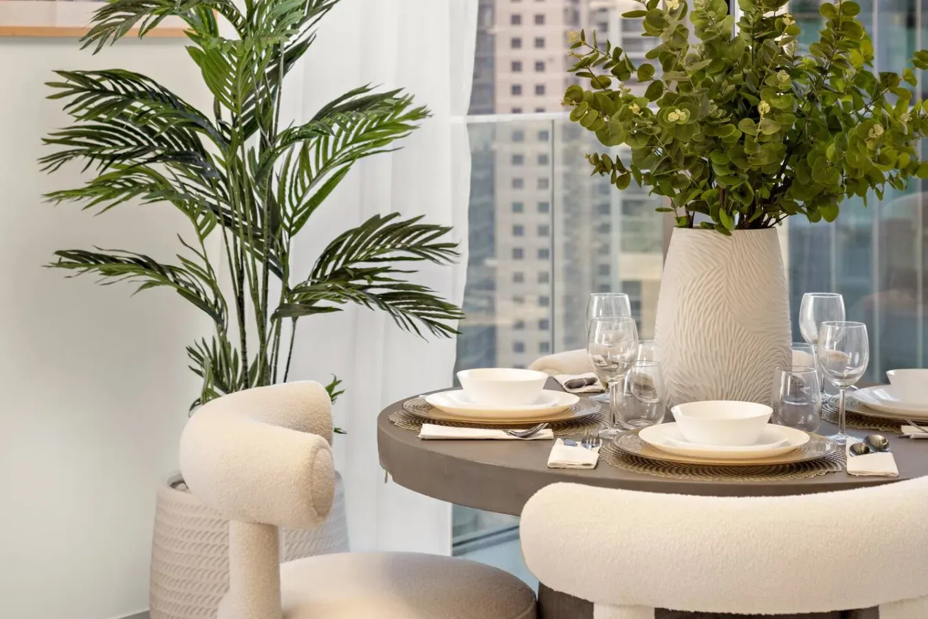 A dining table set with dishes and glassware sits beside a large window.