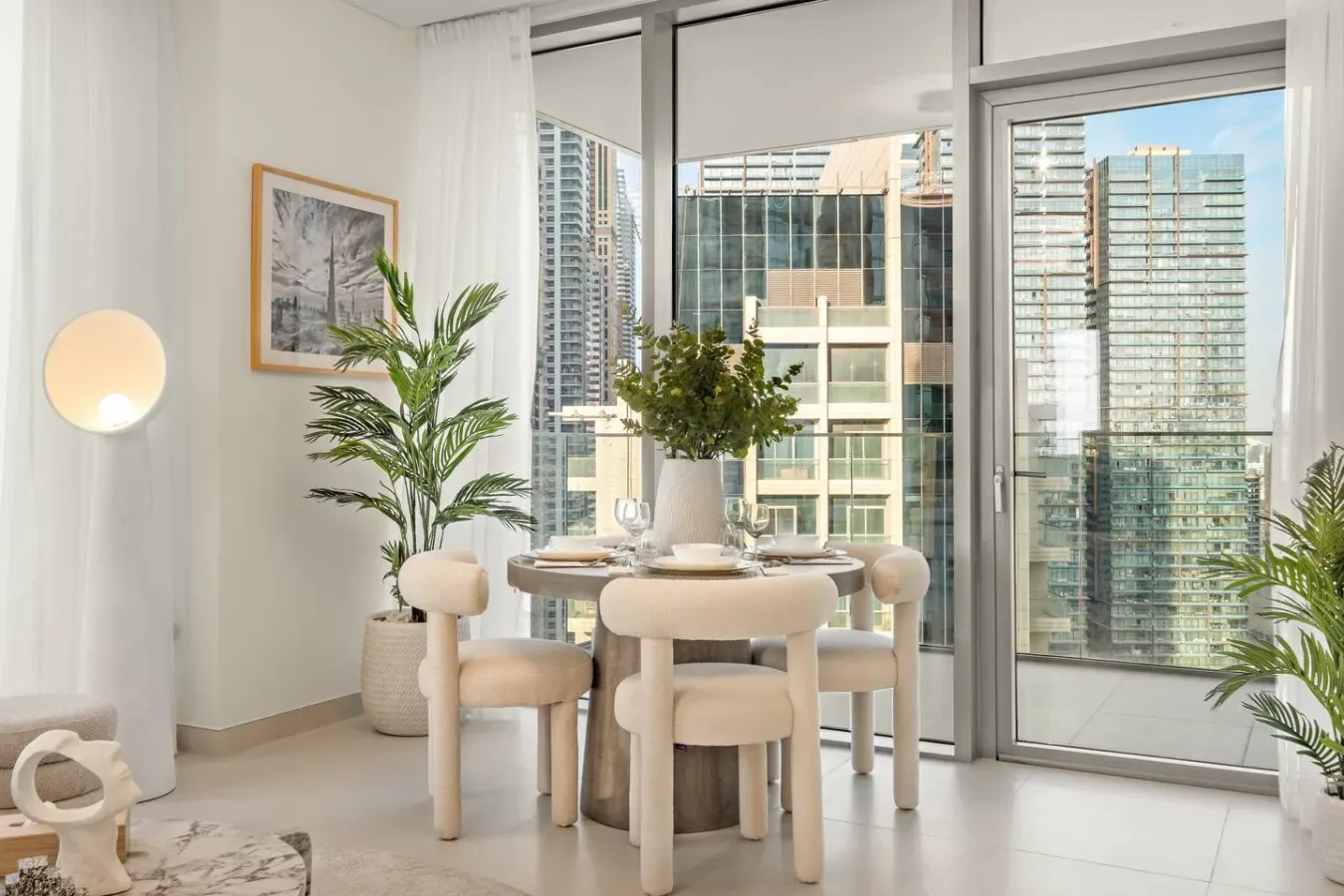 A bright dining area with a round table and large windows overlooking nearby buildings.