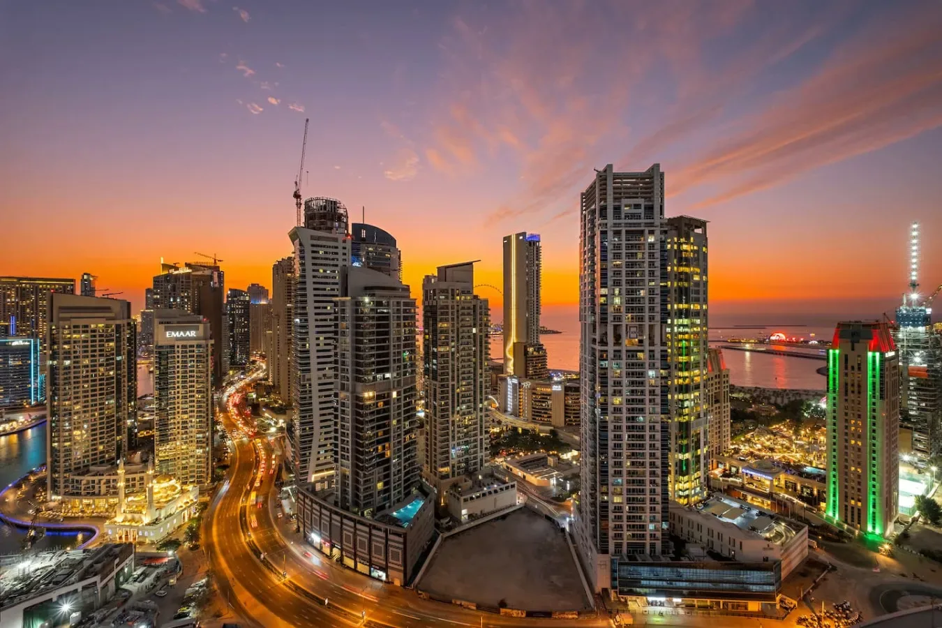 Horizonte urbano al atardecer, con edificios altos iluminados y una carretera curva.