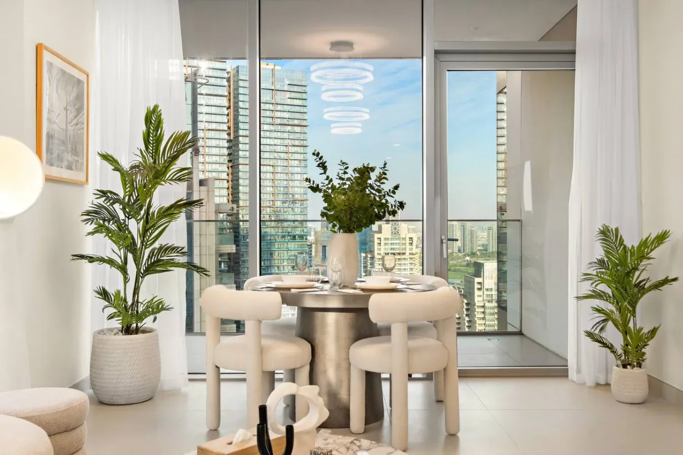Un comedor luminoso con una mesa redonda y grandes ventanales con vistas a edificios cercanos.