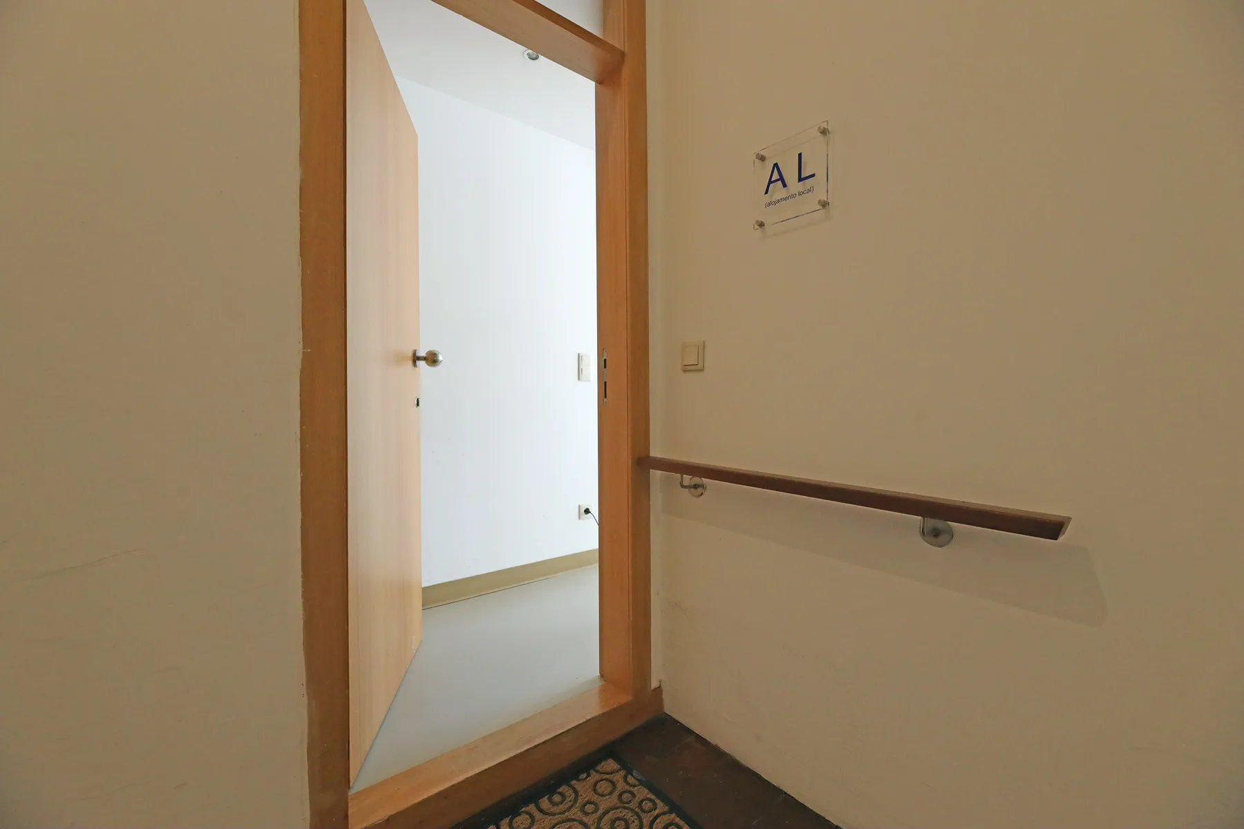 An open doorway leads into a bright interior hallway with a wall handrail.