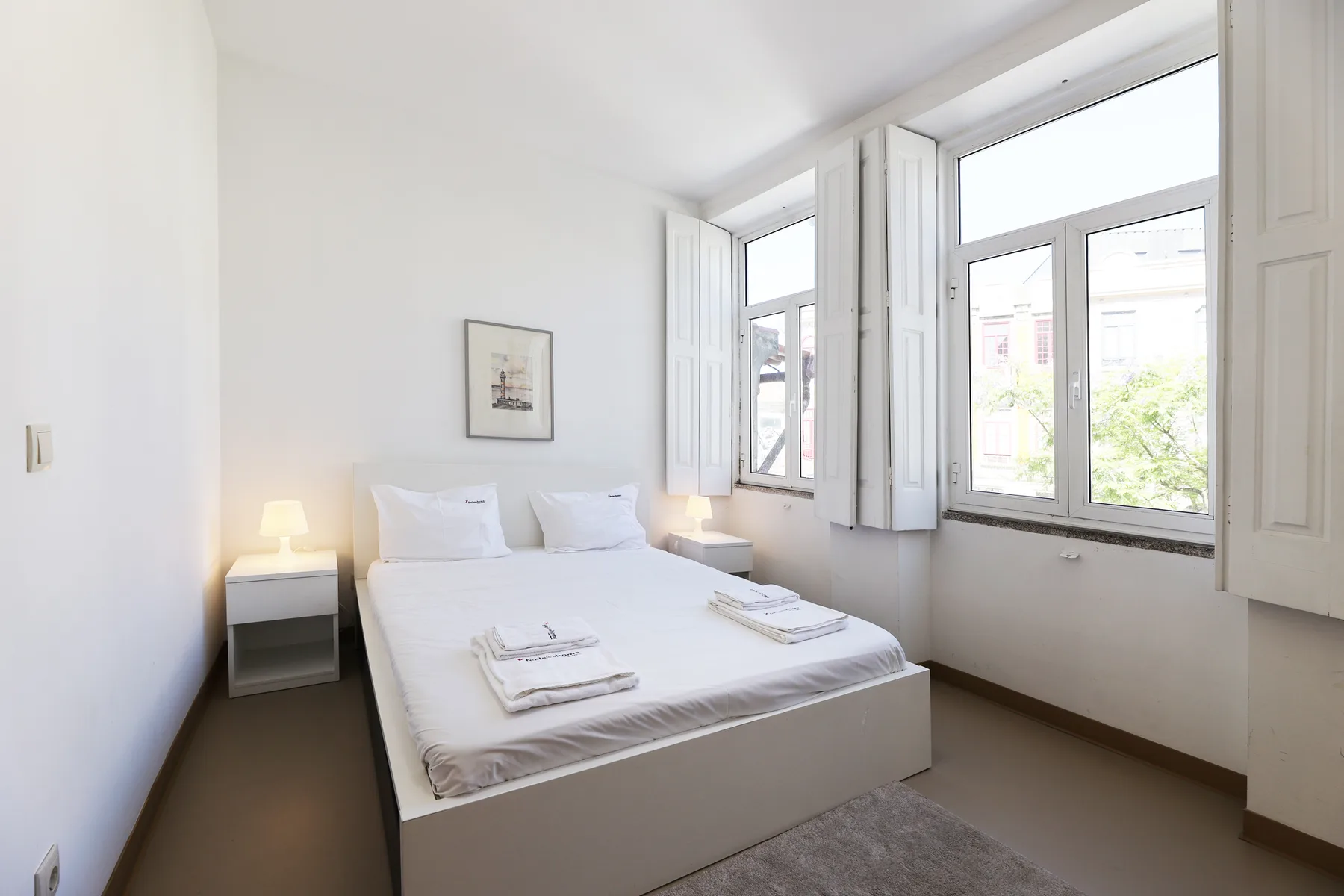 A bright bedroom with a neatly made bed beside large windows.