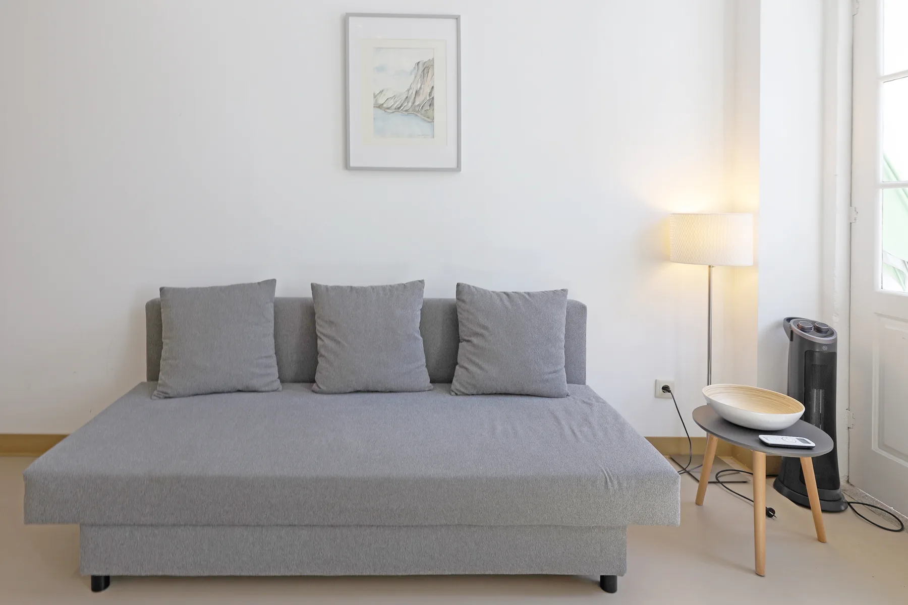 A bedroom with a gray bed, framed picture, and floor lamp.