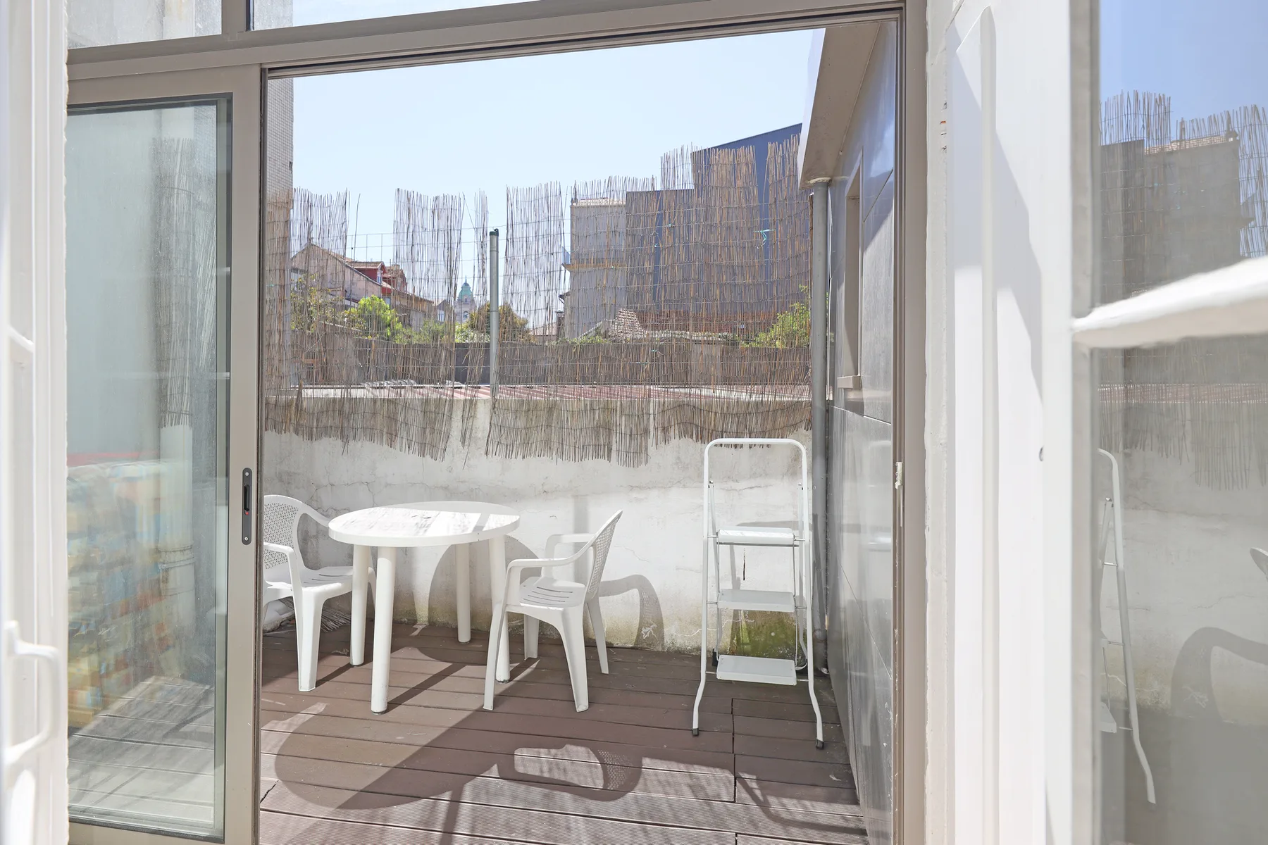 A small balcony has a round table and white outdoor seating.