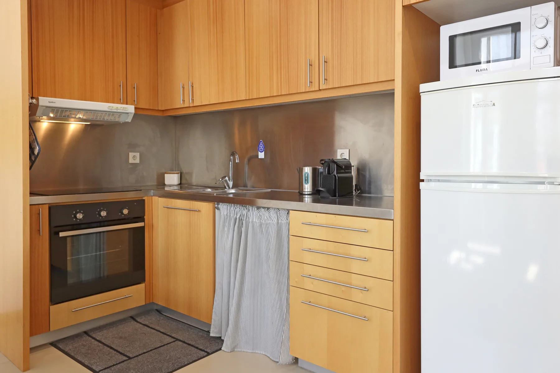 A compact kitchen with wooden cabinets, countertop appliances, and a built-in oven.
