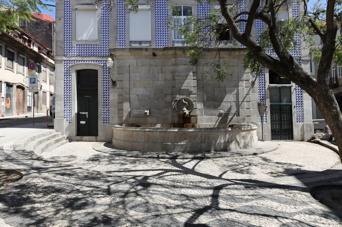 A stone fountain stands beside a paved street in front of a tiled building.