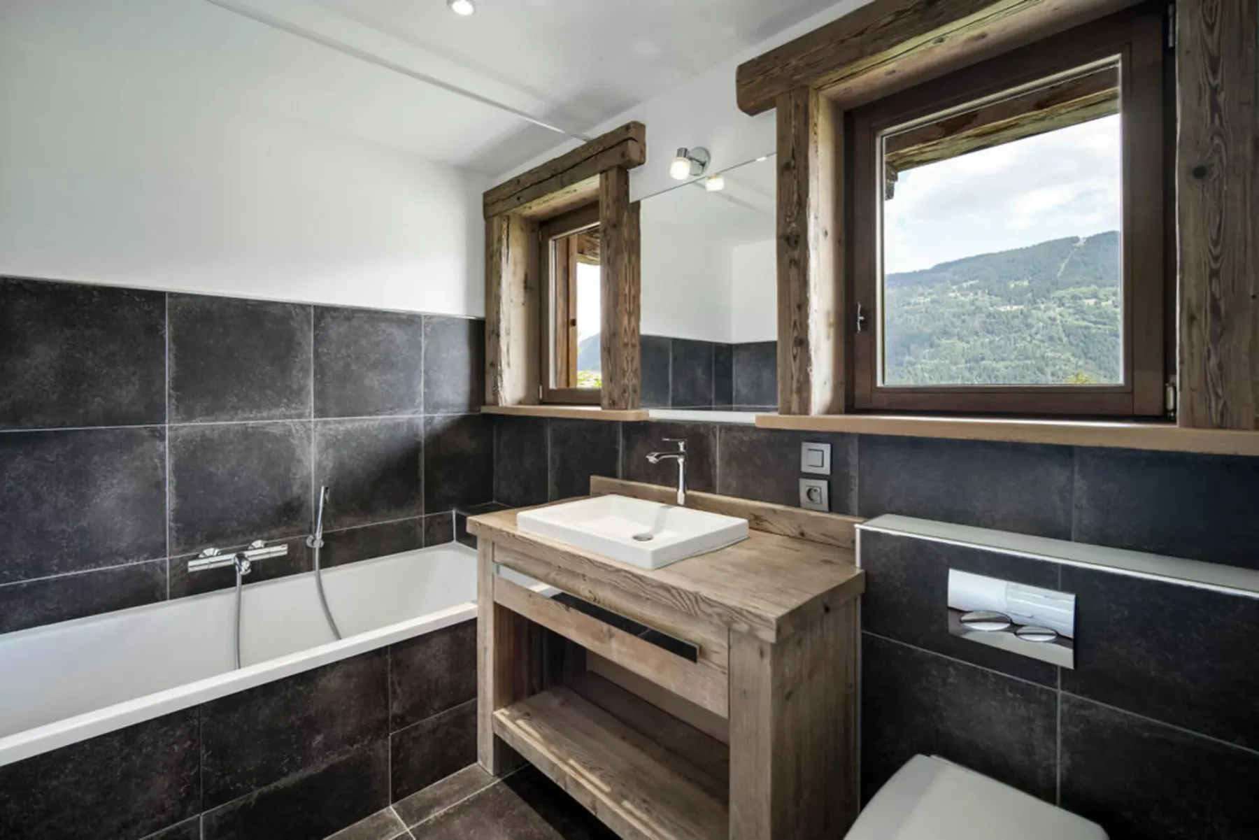 A bathroom with a bathtub, a wood vanity, and windows overlooking a hillside.