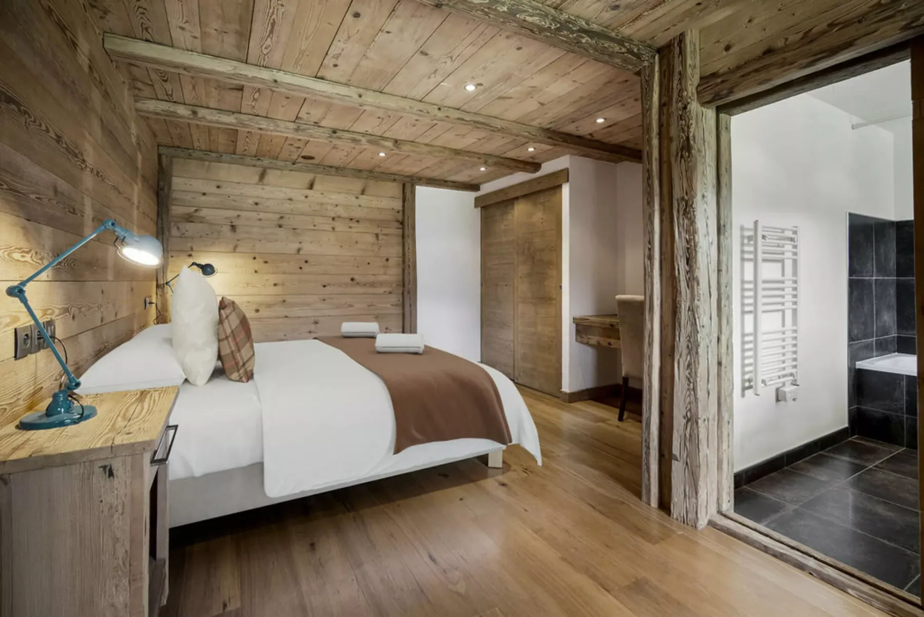 A wood-paneled bedroom with a neatly made bed and an open bathroom doorway.